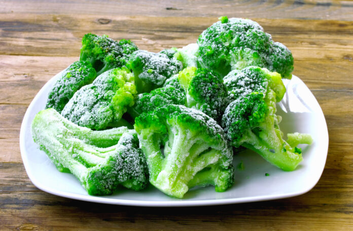 Fresh frozen broccoli on white plate, wooden table, healthy diet food, closeup