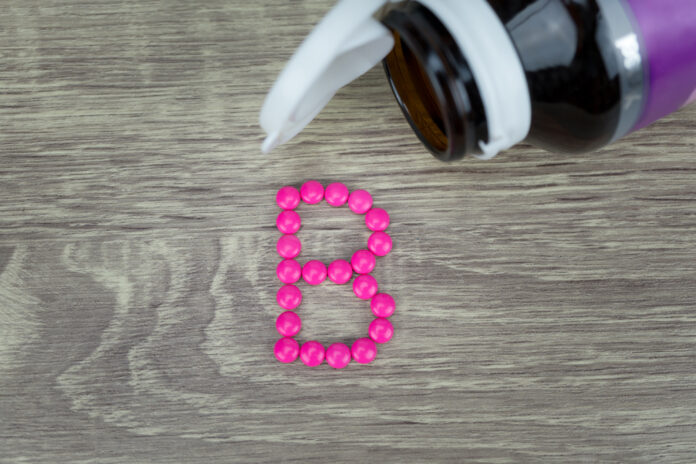 Pink pills forming shape to B alphabet on wood background
