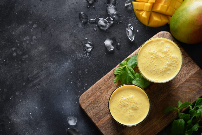 Two Mango lassi or smoothies on black background, top view with copy space. Indian traditional cold mango lassi made of yogurt, water, spices, fruits and ice.