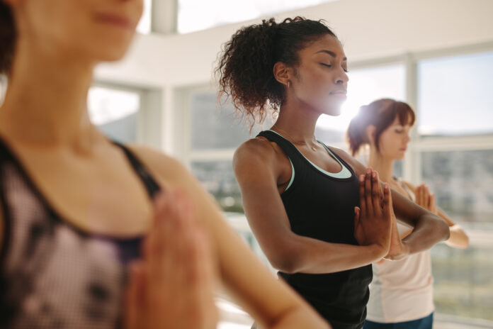 Jeune femme en forme pratiquant le yoga avec des amis. Femme en forme faisant du yoga et de la méditation à l'intérieur dans une salle de gym.