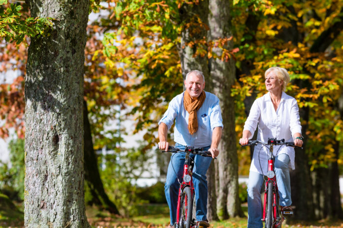 Senior couple, man and woman, on bicycles having bike tour in autumn park