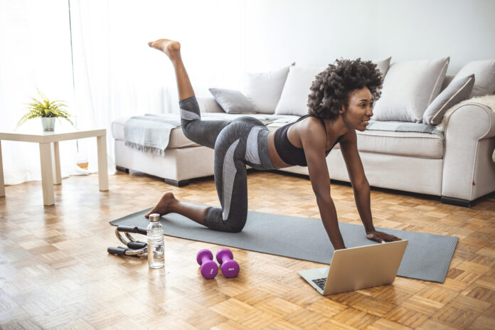 Young beautiful woman exercising at home, fitness concept. Young black woman sitting on the floor at home stretching. Young healthy beautiful woman in sportive top and leggings practicing yoga at home