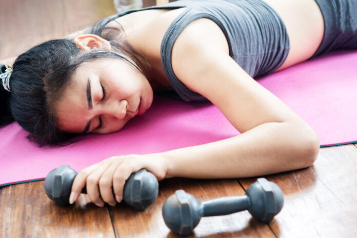 Asian woman lying down on floor feeling tired after doing sport, overtraining hand holding the dumbbell