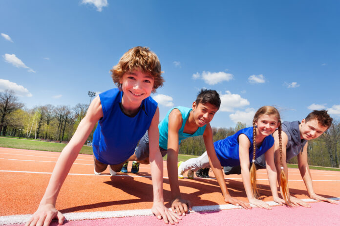 Close-up picture of four happy teenagers in sportswear holding a plank standing in a row  on the track outdoors