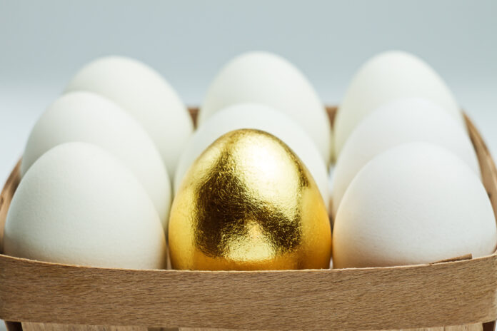 One golden egg among white eggs in a wooden box. Uniqueness concept.