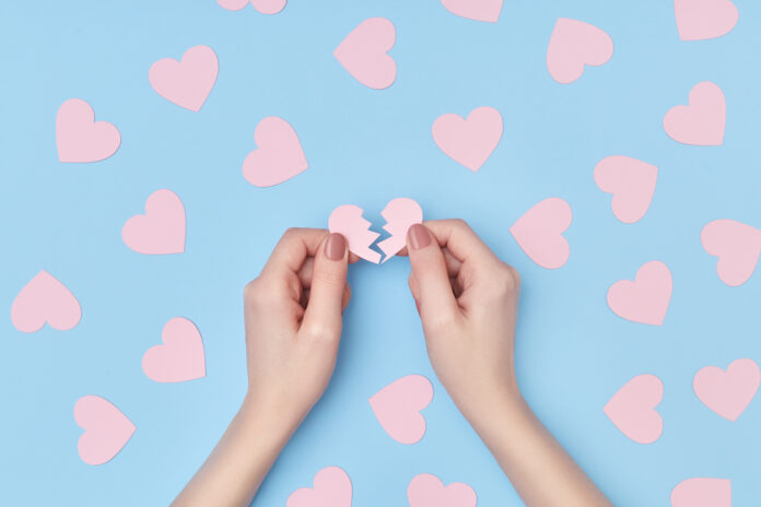 Pattern of pink paper hearts and one broken heart in female hands