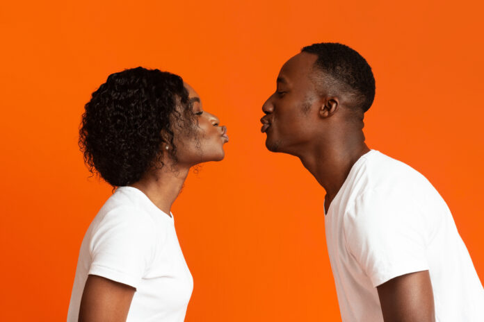 Side view of black man and woman drawn to each other to make kiss over orange studio background, copy space. Love, emotions, feelings concept. African american lovers showing their love