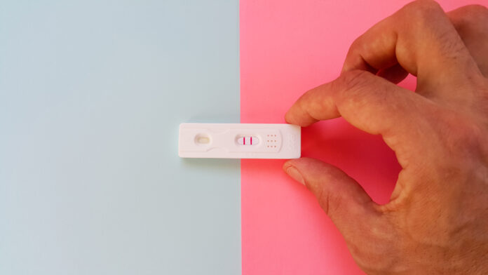 The hand shows the HCG test on a blue and pink background and shows two red lines. A pregnancy test. A positive result. I'm planning a baby. The concept of a boy or a girl. Fertilization and birth.