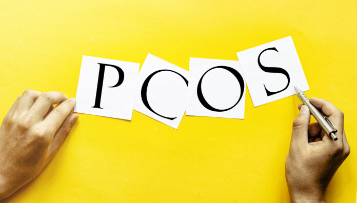 white paper with text PCOS - Polycystic ovary syndrome on a yellow background with man's hands