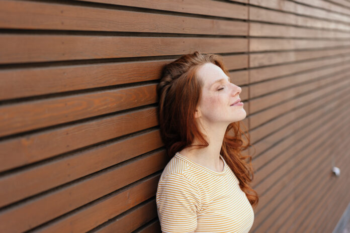 Young woman enjoying a relaxing moment standing with closed eyes leaning against a wall in town with a blissful smile