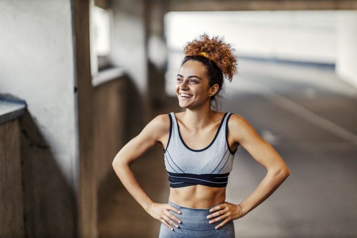 A happy fit urban runner is standing under the underpass with her hands on hips and smiling. The effort is always worthy if you have a goal. An urban runner resting.