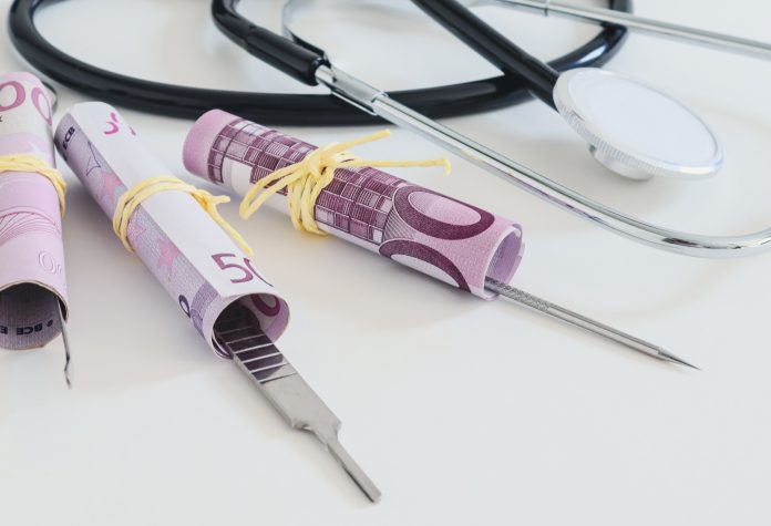 A stethoscope, surgical instruments and three 500 euro bills lie in the middle on a white background, close-up side view.