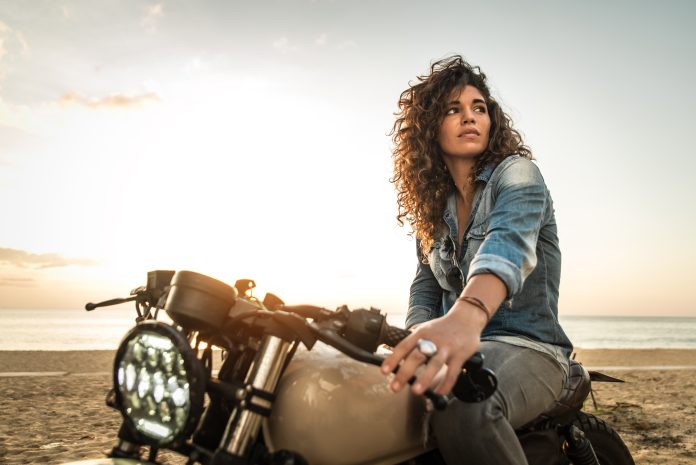 Bella donna motociclista alla guida di una moto cafe' racer - Bella ragazza che guida una moto e si gode il viaggio su strada