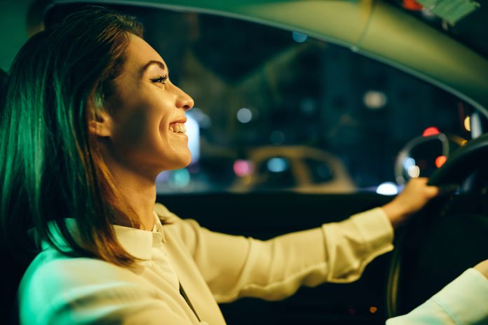 Beautiful happy woman enjoying while driving her car at night.