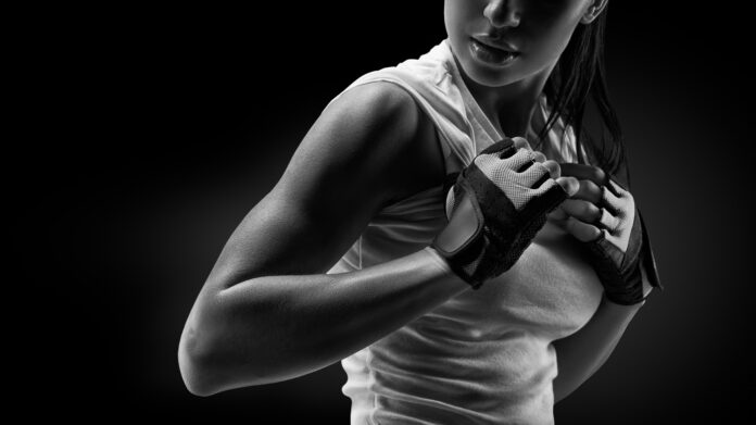 Retrato en blanco y negro de una joven atlética en ropa deportiva mostrando su cuerpo bien entrenado, six pack, abdominales perfectos, hombros, bíceps, tríceps y pecho, músculo deltoides.