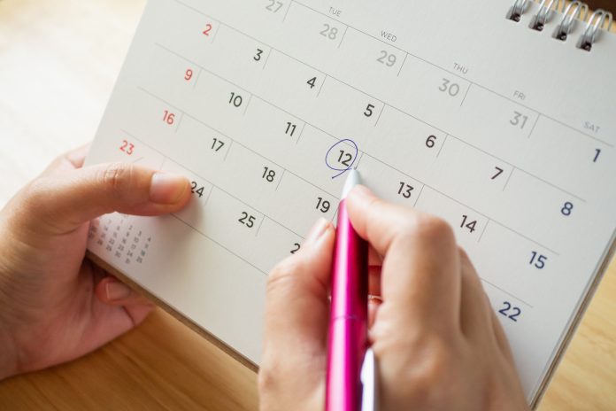 página de calendario con una mano femenina sosteniendo un bolígrafo sobre una mesa de escritorio