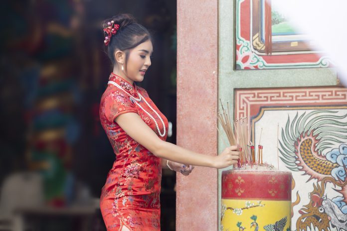 Chinesische Frau in einem roten Cheongsam-Kleid, die Weihrauch hält, huldigt dem chinesischen Gott am Schrein. Konzept zur Feier des chinesischen Neujahrs.