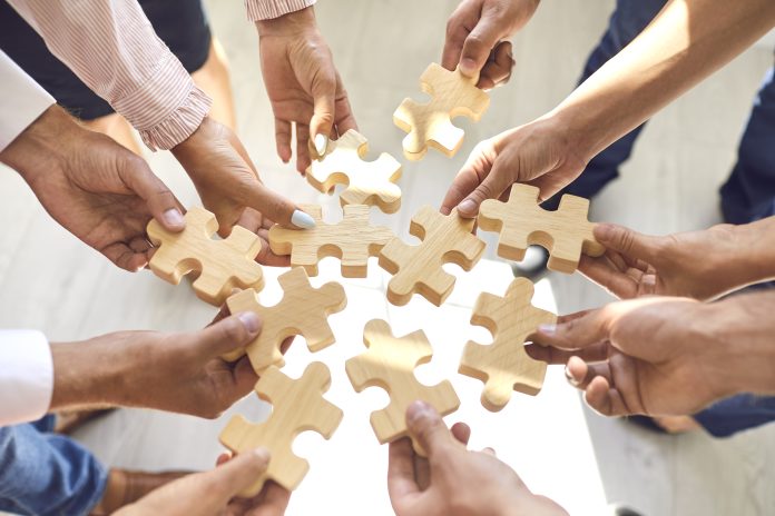 Close up of company workers finding solution in corporate work meeting. Cropped office employees learning to collaborate and playing with pieces of jigsaw puzzle during team building activity