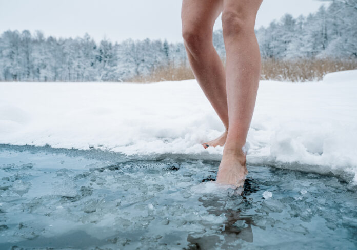 Nahaufnahme der Beine einer Frau, die ins eiskalte Wasser steigt