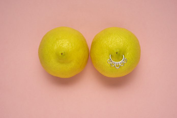 Creative food health fashion concept photo of lemons in shape of woman breast with nipple piercing on pink background.