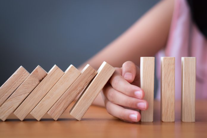 Girl's hand Stopping Falling wooden Dominoes effect from continuous toppled or risk, strategy and successful intervention concept for business and education.