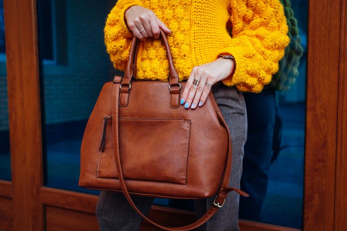 Handtasche. Frau hält stilvolle Tasche und trägt gelben Pullover. Herbst weibliche Kleidung und Accessoires. Modisches Outfit