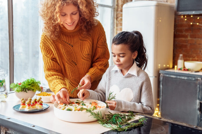 Happy curly woman and mulatto girl niece making healthy vegan salad and snacks for family feasting. Christmas, New year, Thanksgiving, Anniversary, Hanukkah, Mothers day, Easter, engagement concept