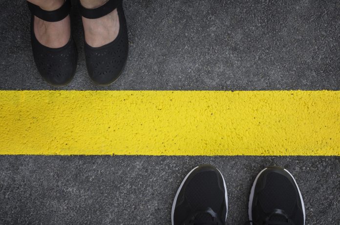 Gambe di una coppia in piedi una di fronte all'altra divise dalla linea gialla dell'asfalto vista dall'alto