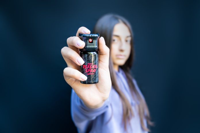 Self defence of young teenager girl with pepper spray. Isolated on dark background.