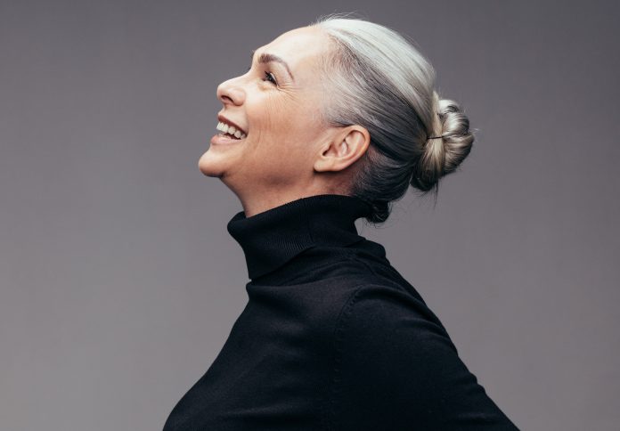 Side view of senior woman laughing on gray background. Profile view of mature woman in black casuals looking happy
