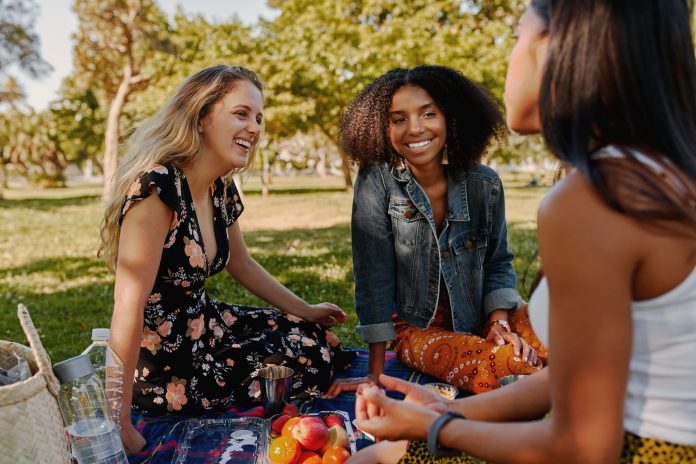 Lächelnde multirassische Freundinnen, die sich beim Picknick im Park amüsieren - Gruppe gesunder Freunde beim Picknick
