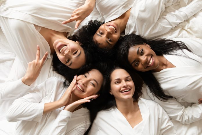 Vista dall'alto cinque donne diverse in accappatoi bianchi sdraiate nel letto sorridono guardando la macchina fotografica si sentono felici dopo il trattamento del corpo, procedure day spa, salone di bellezza resort clienti soddisfatti, concetto di addio al nubilato