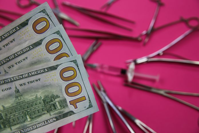 View on 100 us dollar paper bill notes. surgical steel instruments and hyaluronic acid syringe on pink background