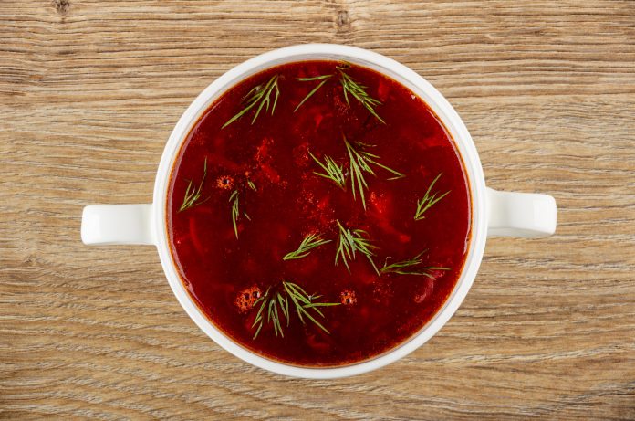 Borscht with dill in white bowl on wooden table. Top view