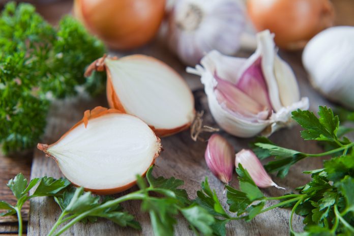 Garlic cloves, shallots and white onions   -  food ingredient on wooden board, decorated with  fresh parsley.