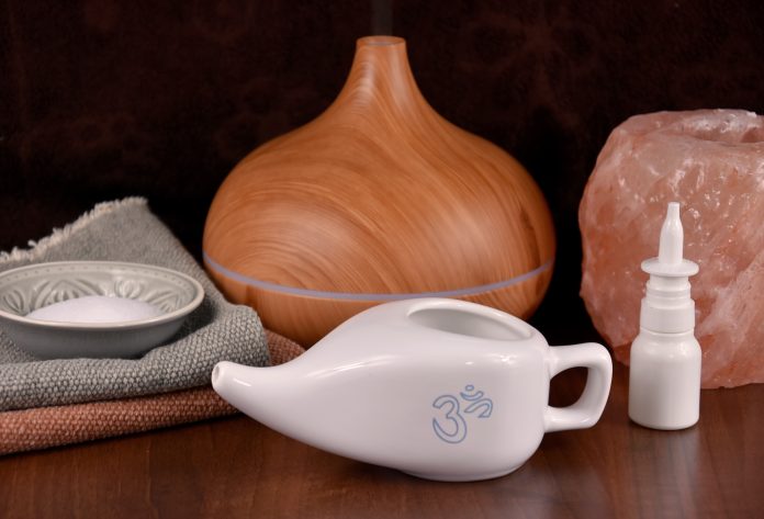 Nasal care images. White ceramic Neti pot with OM symbol stock photo. Neti pot still life with wooden humidifier, salt lamp and nasal spray images