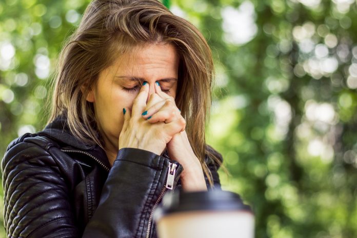 Tired young woman with brown hair bowing her head while holding it with her index fingers in nature – Girl having headache and sinuses pain