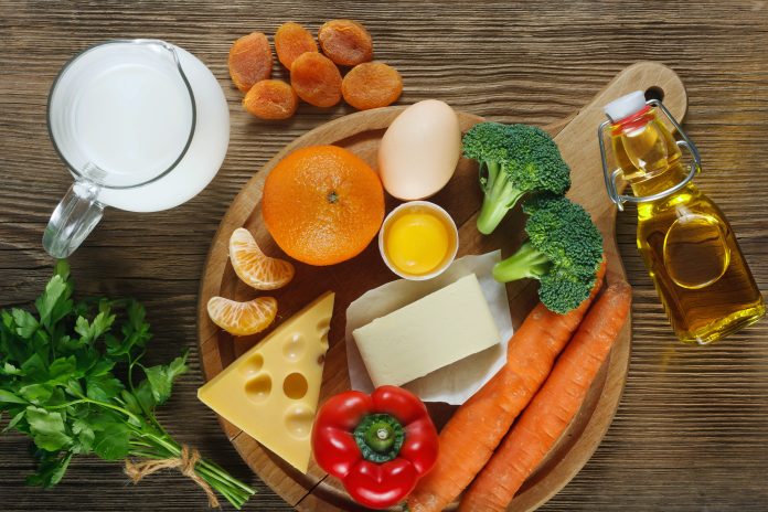 Vitamin A in food. Natural products rich in vitamin A as tangerine, red pepper, parsley leaves, dried apricots, carrots, broccoli, butter, yellow cheese, milk, egg yolk and cod liver oil. Wooden table as background.
