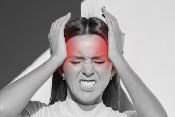 Young woman touching her temples and having strong tension headache. Cluster headache. Female suffering from migraine, stress, hangover with red alert accent. Hands on head. High quality photo