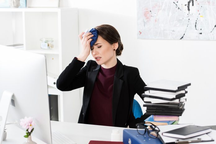 businesswoman having headache and touching head with ice pack in office
