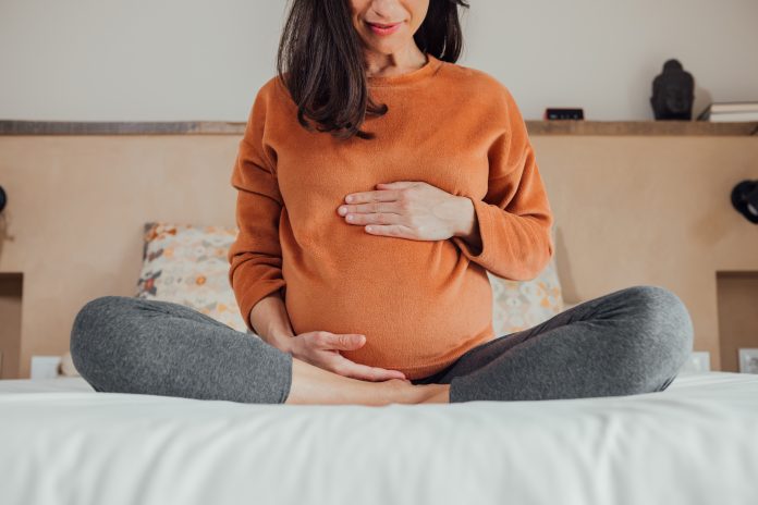 Cropped Pregnant woman, sitting in crossed legs in be at home holding her belly.