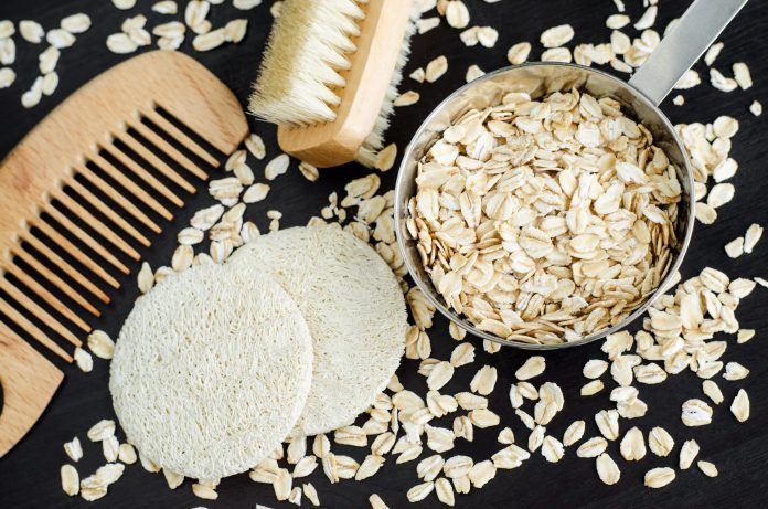 Small bowl with oatmeal, loofah sponges and wooden hairbrush. Homemade hair or face mask, natural beauty treatment and spa recipe. Top view, copy space.