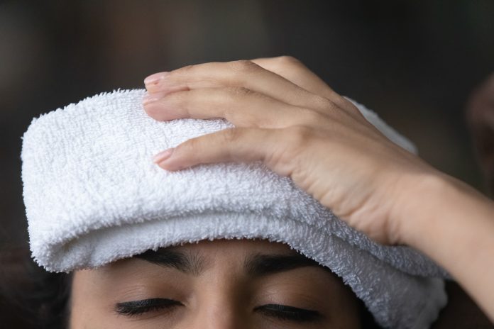 Sick young female having fever holding wet towel on head
