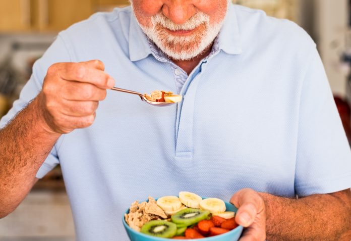 Smiling elderly man holding a bowl of fresh and dried fruits. Breakfast or lunch time, healthy eating