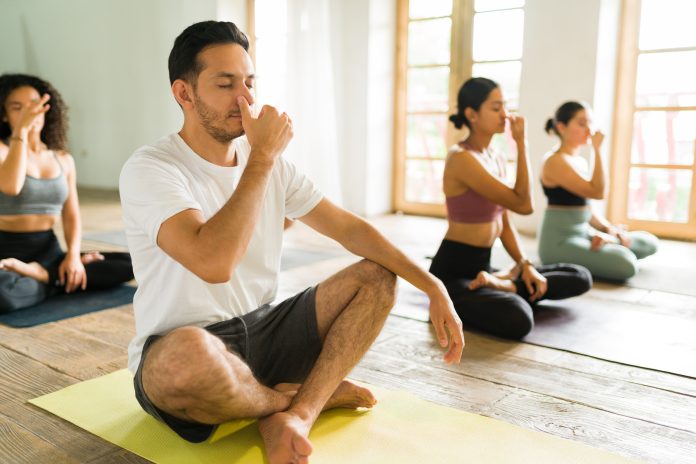 relaxing with eyes closed while doing breathing exercises and meditating at a yoga class